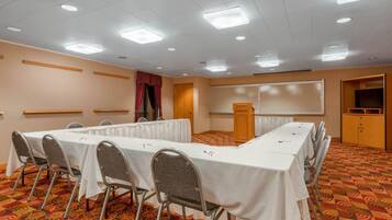 Un salón de conferencias con una larga mesa, sillas, un atril y una pantalla de proyección.