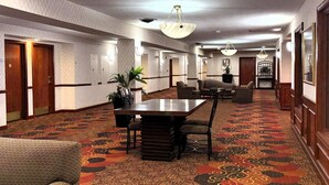 Un vestíbulo de hotel con un largo pasillo, puertas de madera, una gran mesa de conferencias y varias sillas.