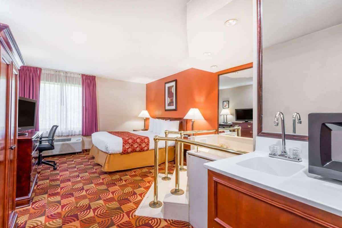 Habitación de hotel con cama, escritorio, silla, televisión y baño.