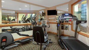 Un gimnasio con diversos equipos de ejercicio, incluyendo cintas de correr y bicicletas estáticas, y un espejo grande que refleja el espacio.