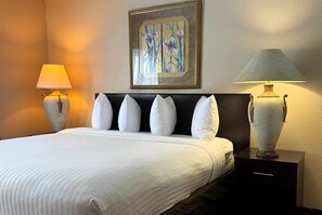 Una habitación de hotel con cama, dos lámparas de noche, una mesita de noche y un cuadro con motivos florales en la pared.