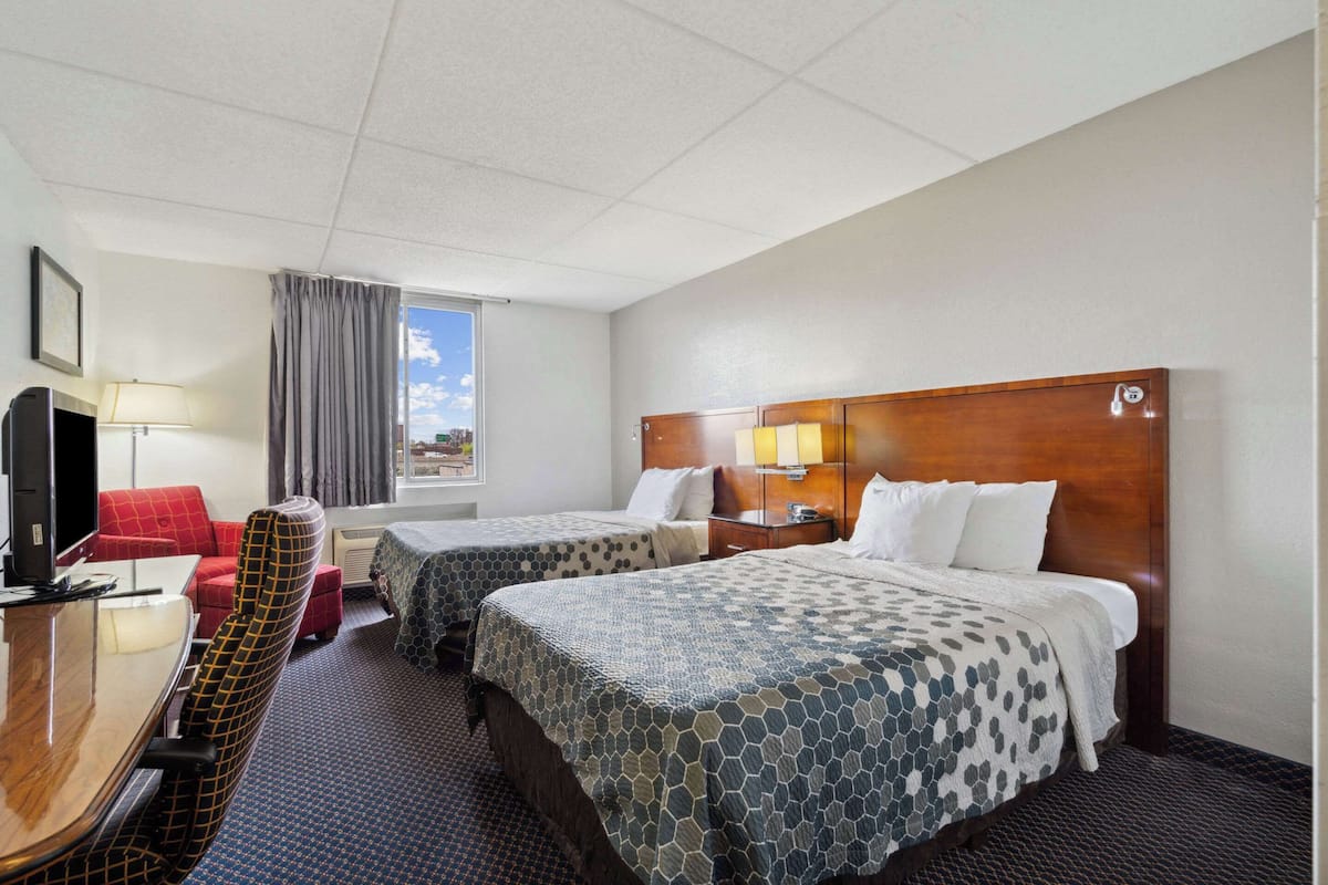 A hotel room with two beds, a desk with a chair, a TV, and a window with curtains.