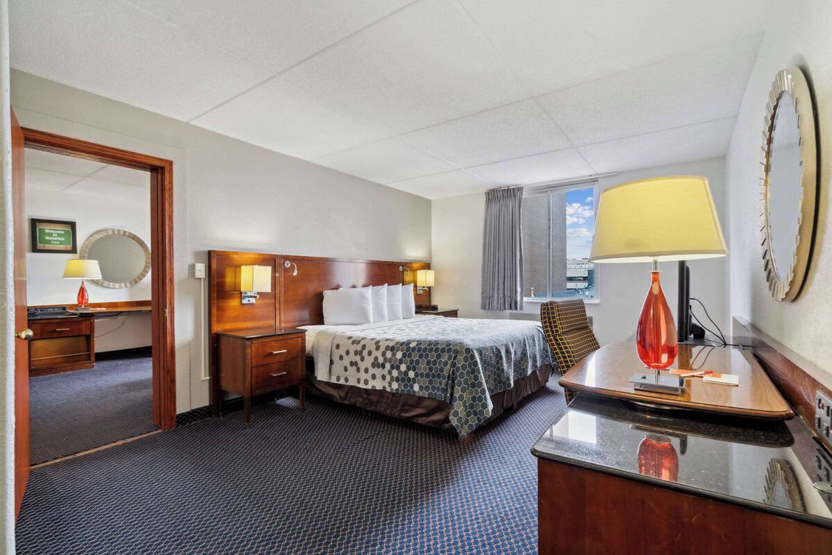 A hotel room with a bed, bedside tables, a desk, a mirror, and a window with curtains.