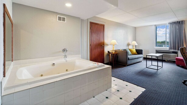 A modern hotel room with a large bathtub, a sofa, a small table, and a window with a view. - Econo Lodge Inn & Suites Waterloo Downtown (Waterloo)