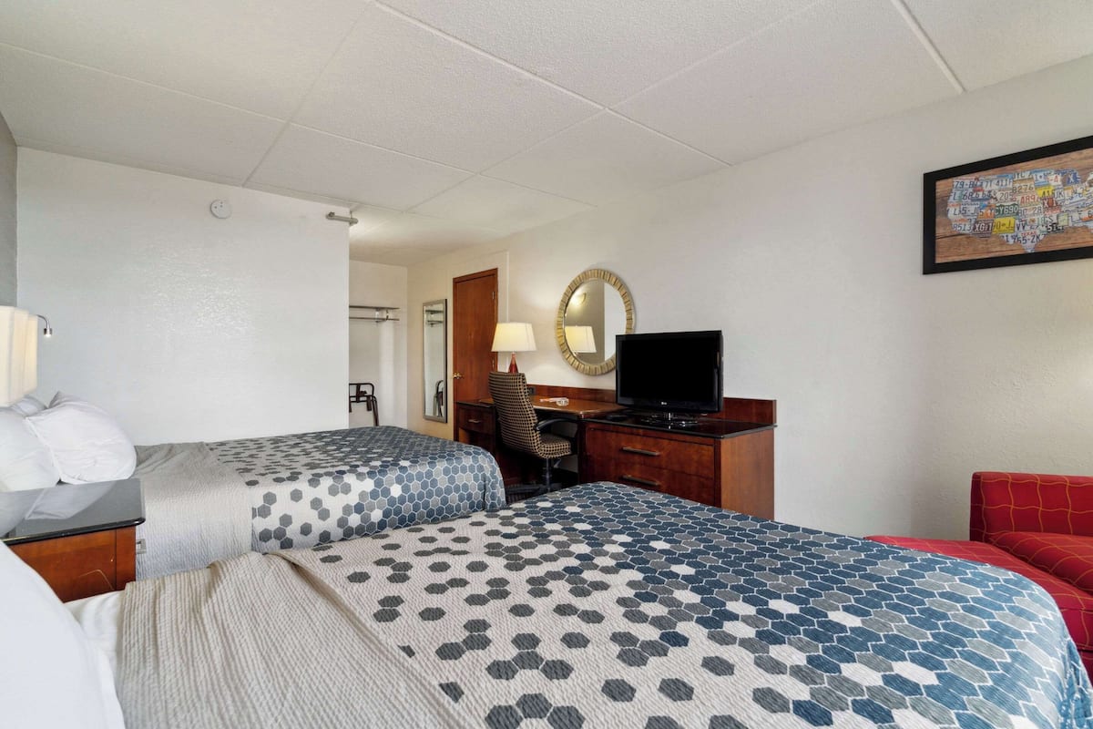 A hotel room with two beds, a desk with a TV, a chair, a mirror, and a map on the wall.