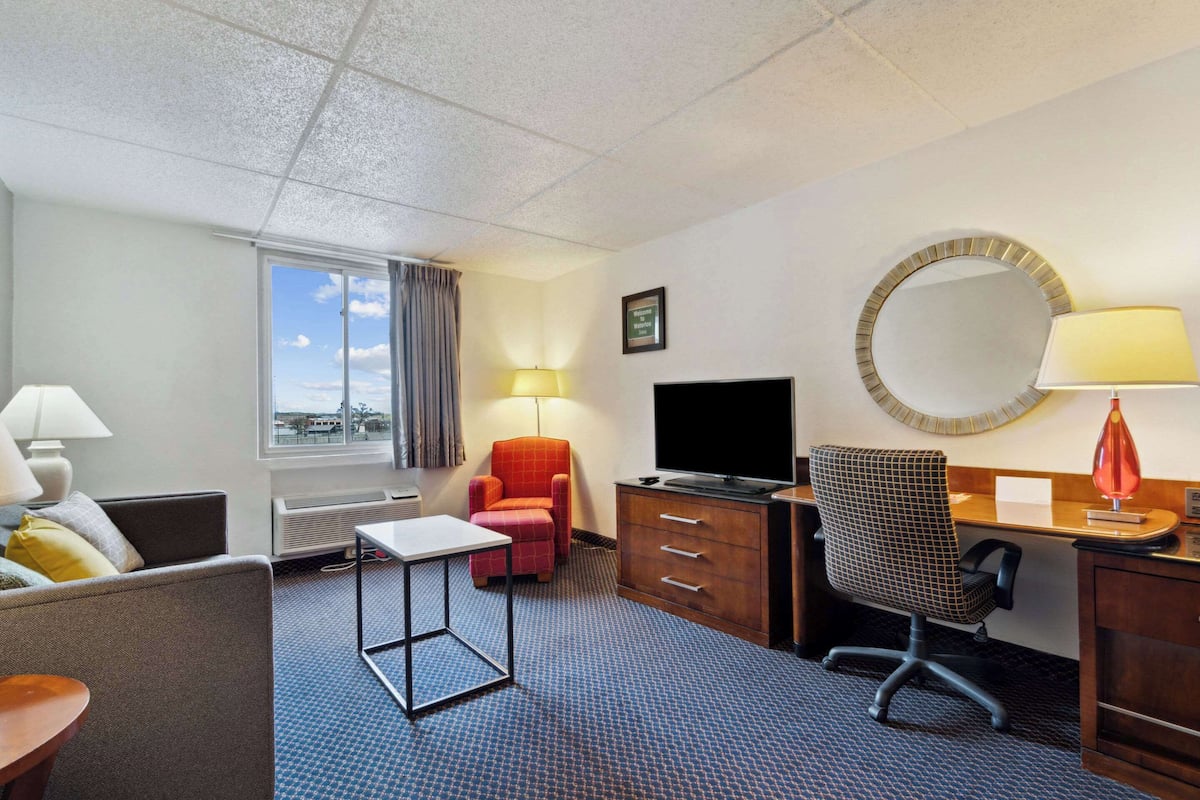 A hotel room with a bed, a desk, a chair, a TV, a mirror, and a window with a view.