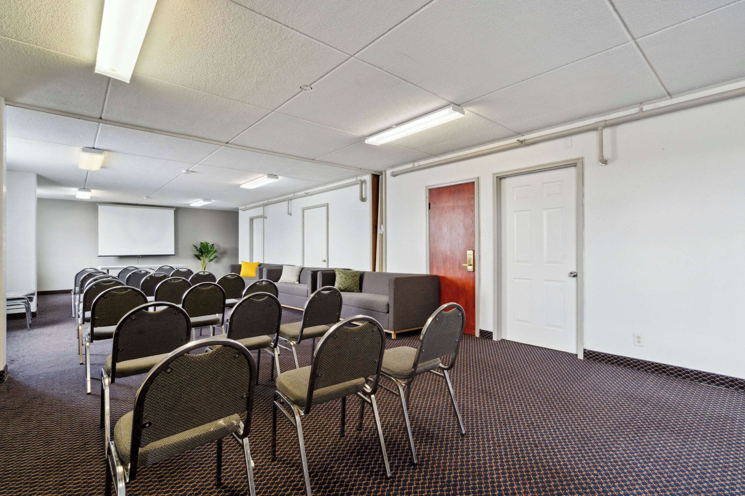 A conference room with rows of chairs, a sofa, a projector screen, and a door.