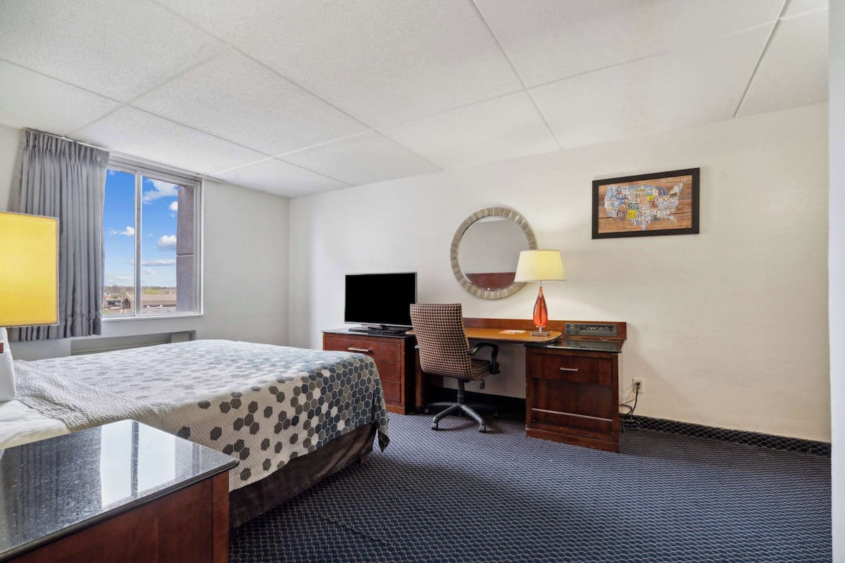 A hotel room with a bed, desk, chair, TV, lamp, and a map on the wall.