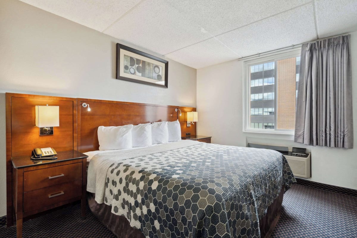 A hotel room with a large bed, two bedside lamps, a framed picture on the wall, and a window with curtains.