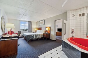 Habitación de hotel con cama, mesita de noche, lámpara y una bañera roja.