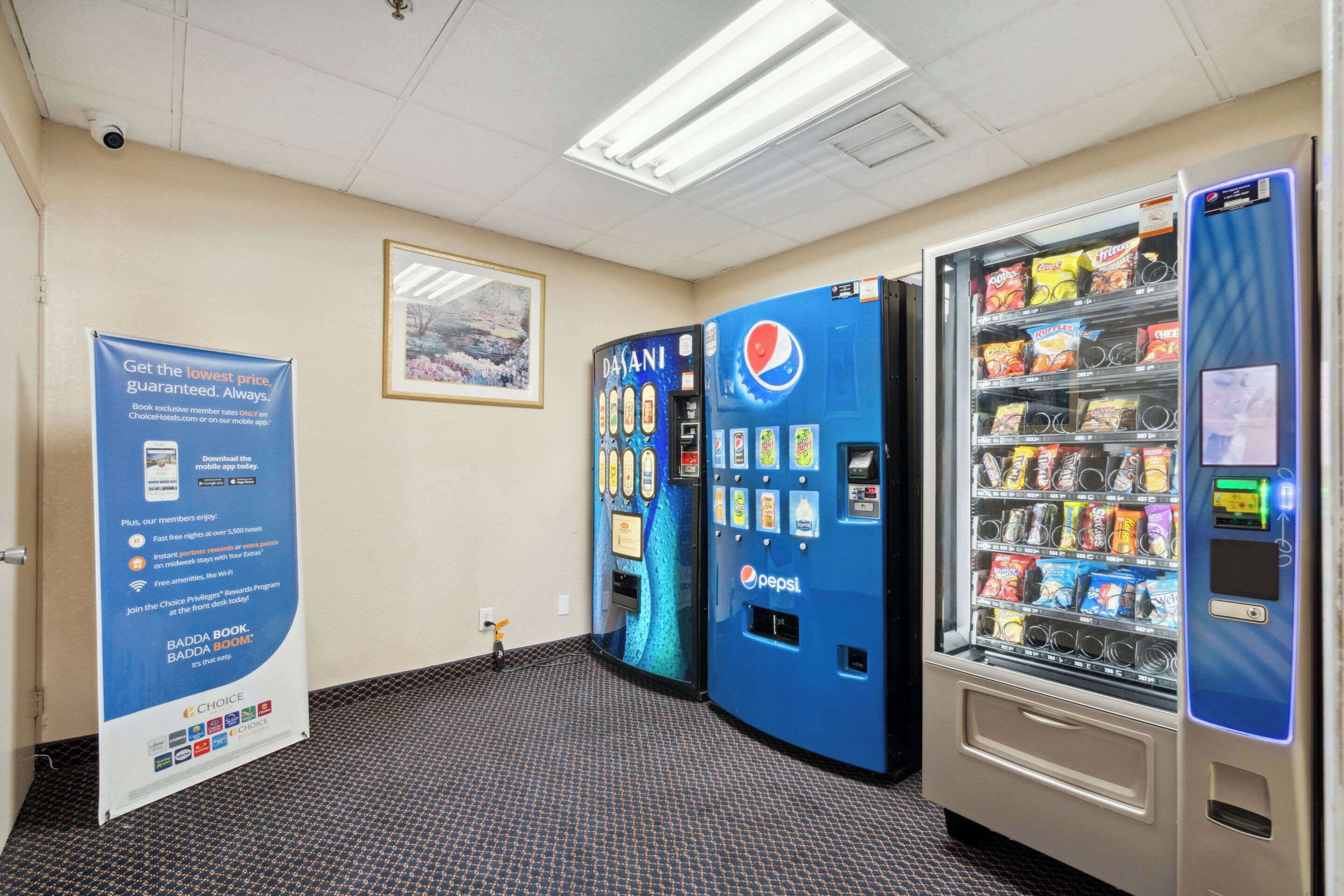 A vending machine area with Pepsi and Dasani water dispensers, a promotional banner, and a framed picture on the wall.