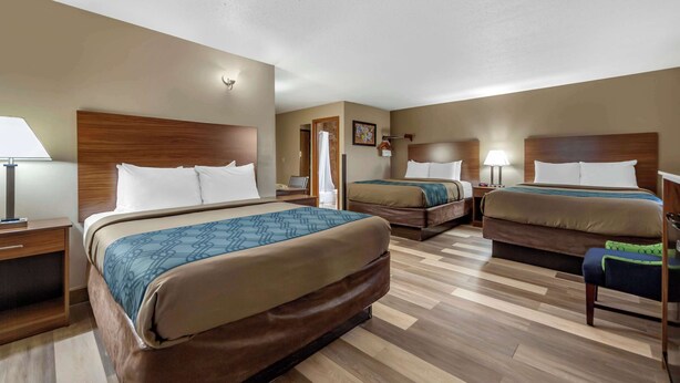 A hotel room with three beds, wooden headboards, and a wooden floor. - Econo Lodge Hays I-70 (Hays)