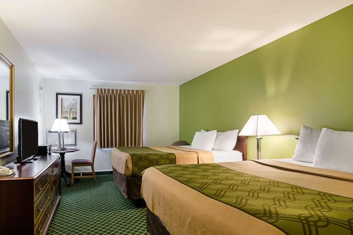 A hotel room with two beds, a desk with a computer, a chair, and a television.