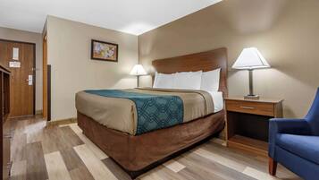 A hotel room with a large bed, two bedside tables with lamps, a wooden headboard, and a blue armchair.