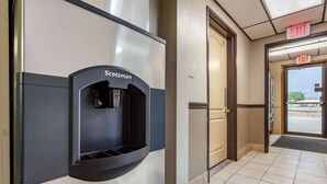 A water dispenser labeled "Scotsman" mounted on a wall, an exit sign above a door, and a tiled floor. - Econo Lodge Hays I-70 (Hays)