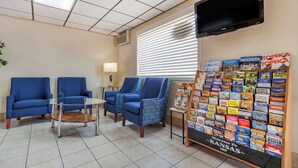 A waiting area with blue chairs, a glass table, a TV mounted on the wall, and a display of travel brochures. - Econo Lodge Hays I-70 (Hays)