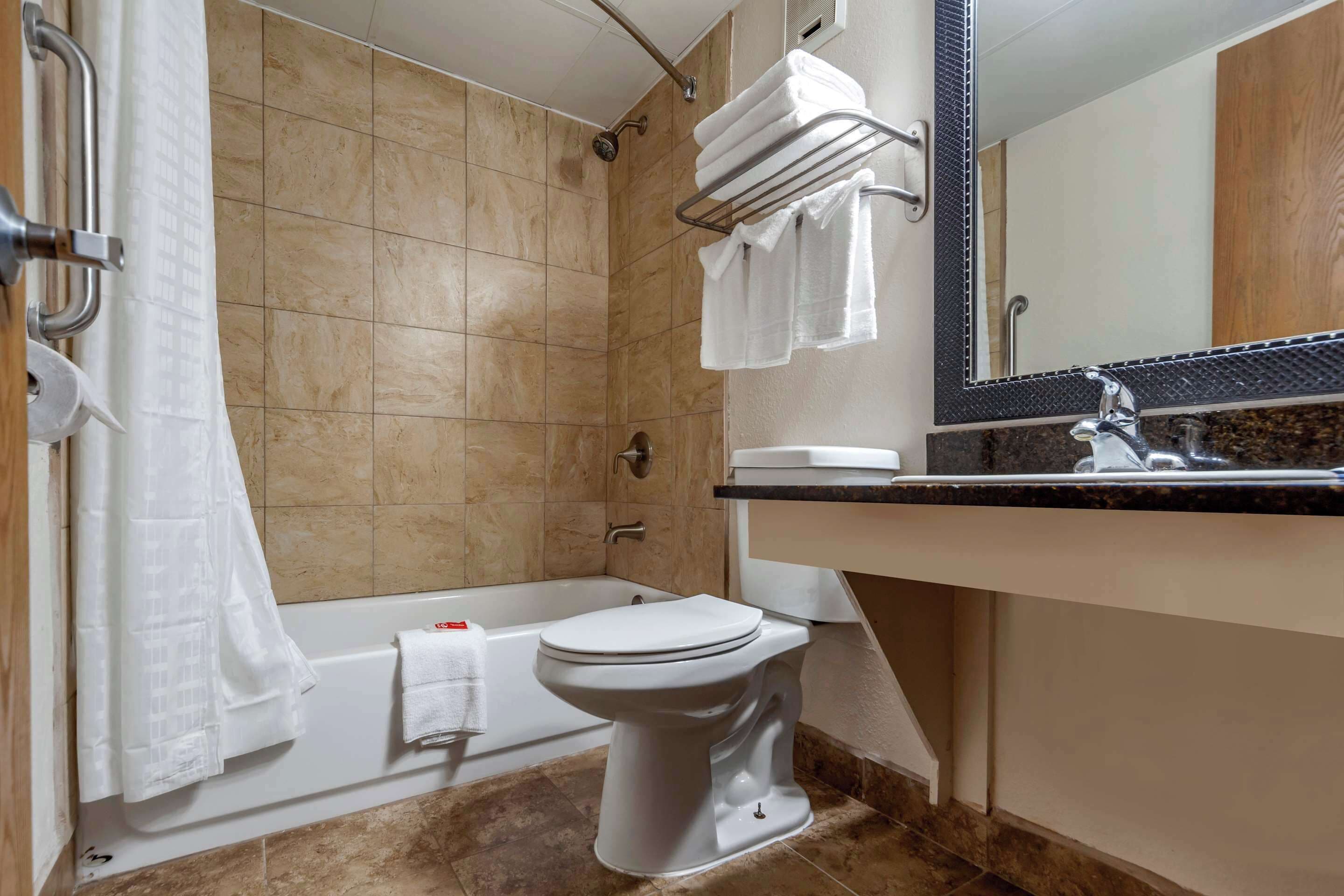 A modern bathroom with a bathtub, toilet, and a large mirror.