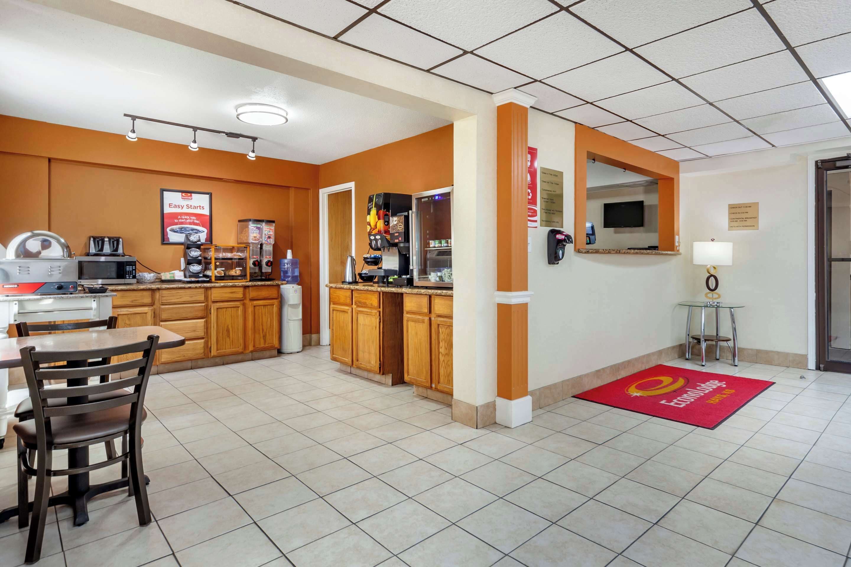 Una cocina de hotel con una máquina de café, un refrigerador y un microondas. Hay una encimera de madera y una mesa con sillas.
