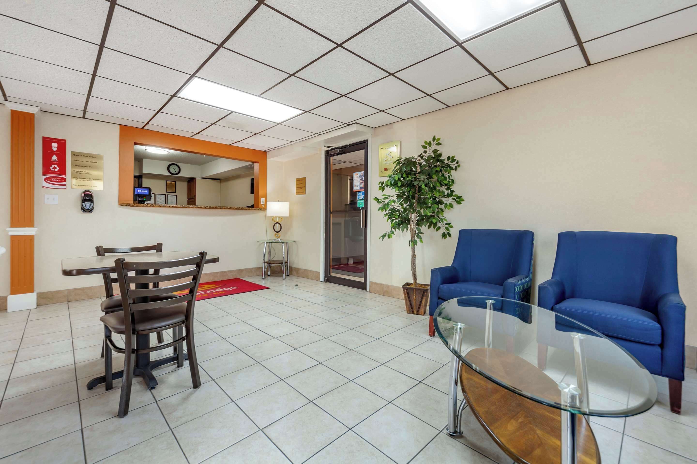 A reception area with a reception desk, a clock, a plant, and blue chairs.