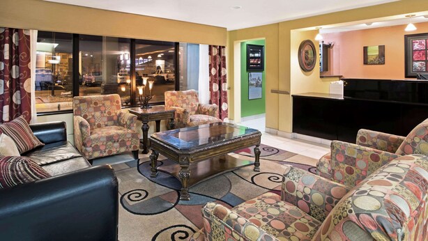 A hotel lobby with a seating area featuring a sofa, armchairs, and a coffee table. There is a reception desk with a television and a framed picture on the wall.