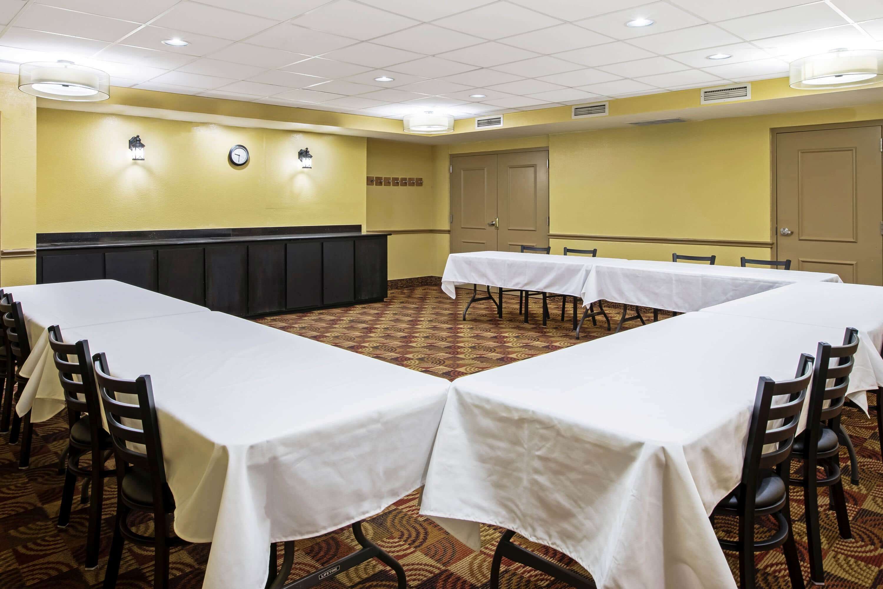 A conference room with long tables and chairs, a clock, and a door.