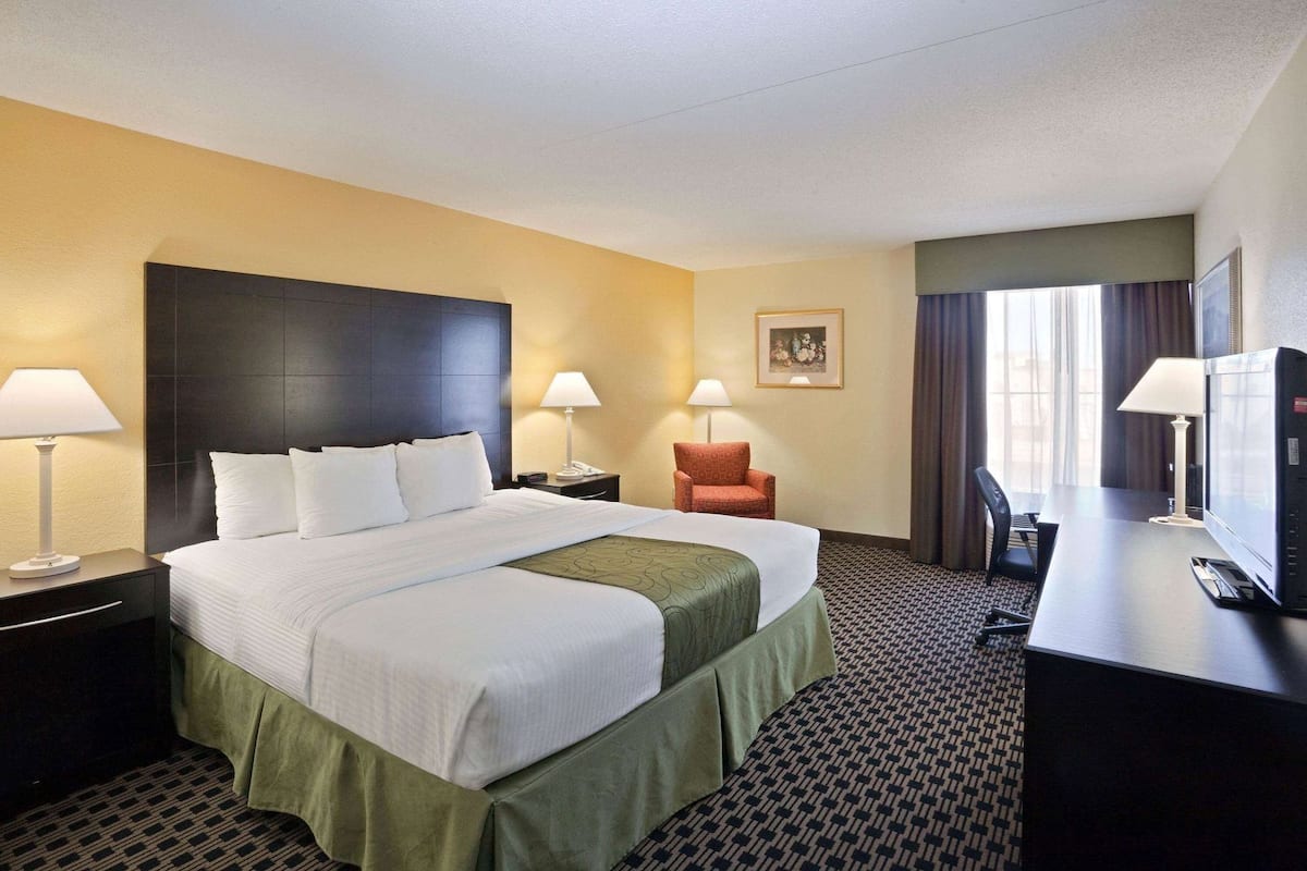 A hotel room with a large bed, two bedside tables with lamps, a desk with a television, a chair, and a painting on the wall.