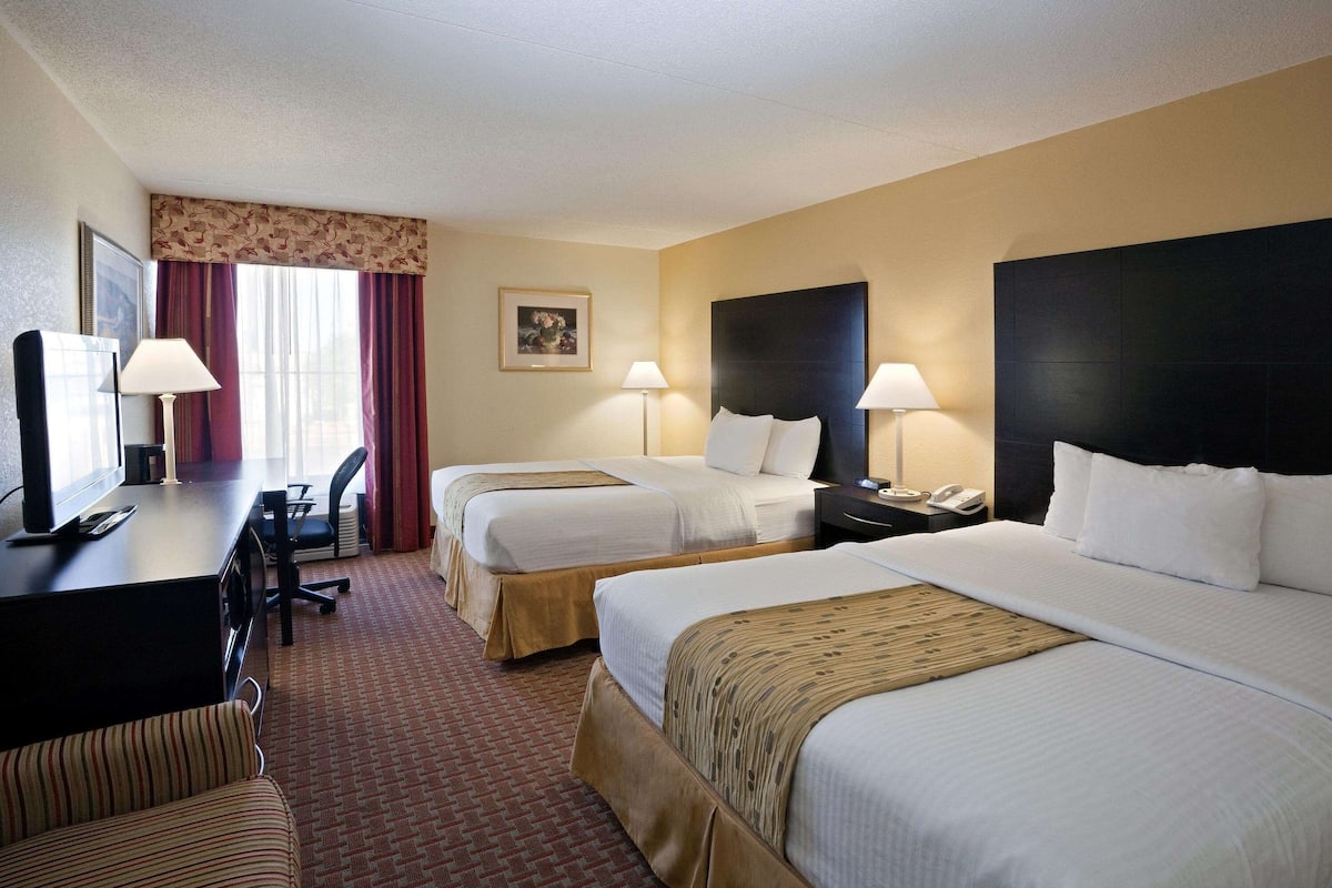 A hotel room with two beds, a desk, a chair, and a television.
