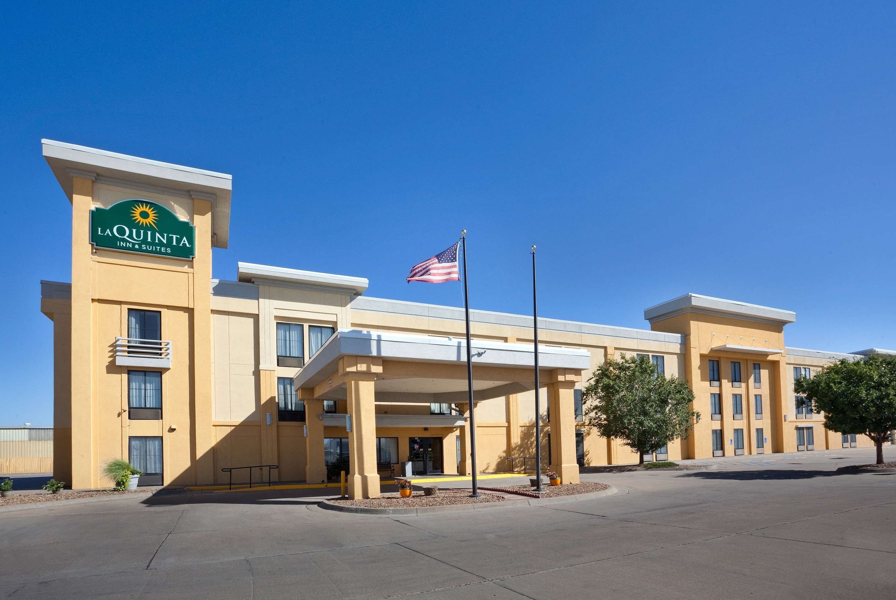 Edificio de La Quinta Inn & Suites con cielo azul despejado, una bandera estadounidense y un estacionamiento.