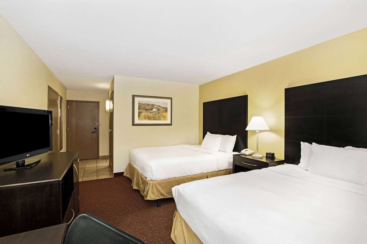 A hotel room with two beds, a TV, a desk, and a painting on the wall.