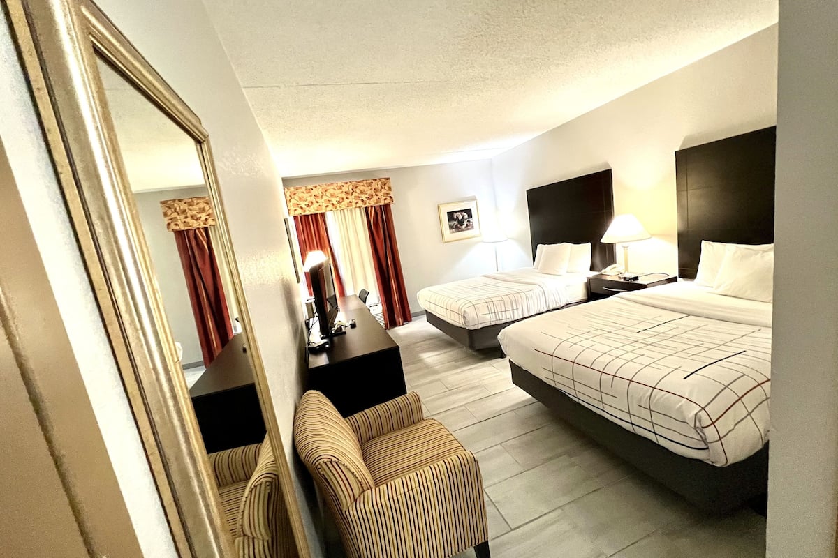 A hotel room with two beds, a desk, a chair, a mirror, and a picture on the wall.