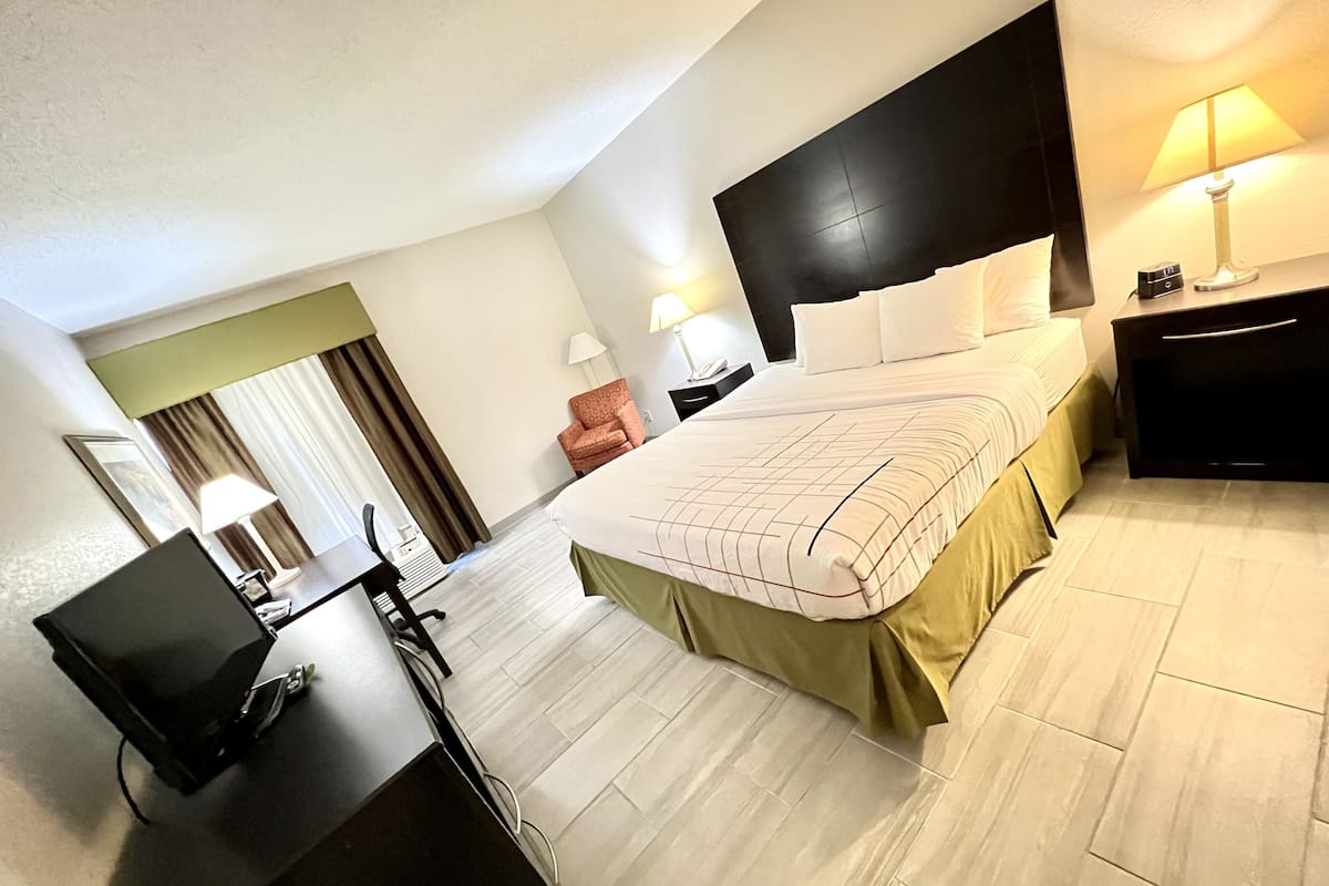 A hotel room with a bed, desk, chair, lamp, and a nightstand with a clock.
