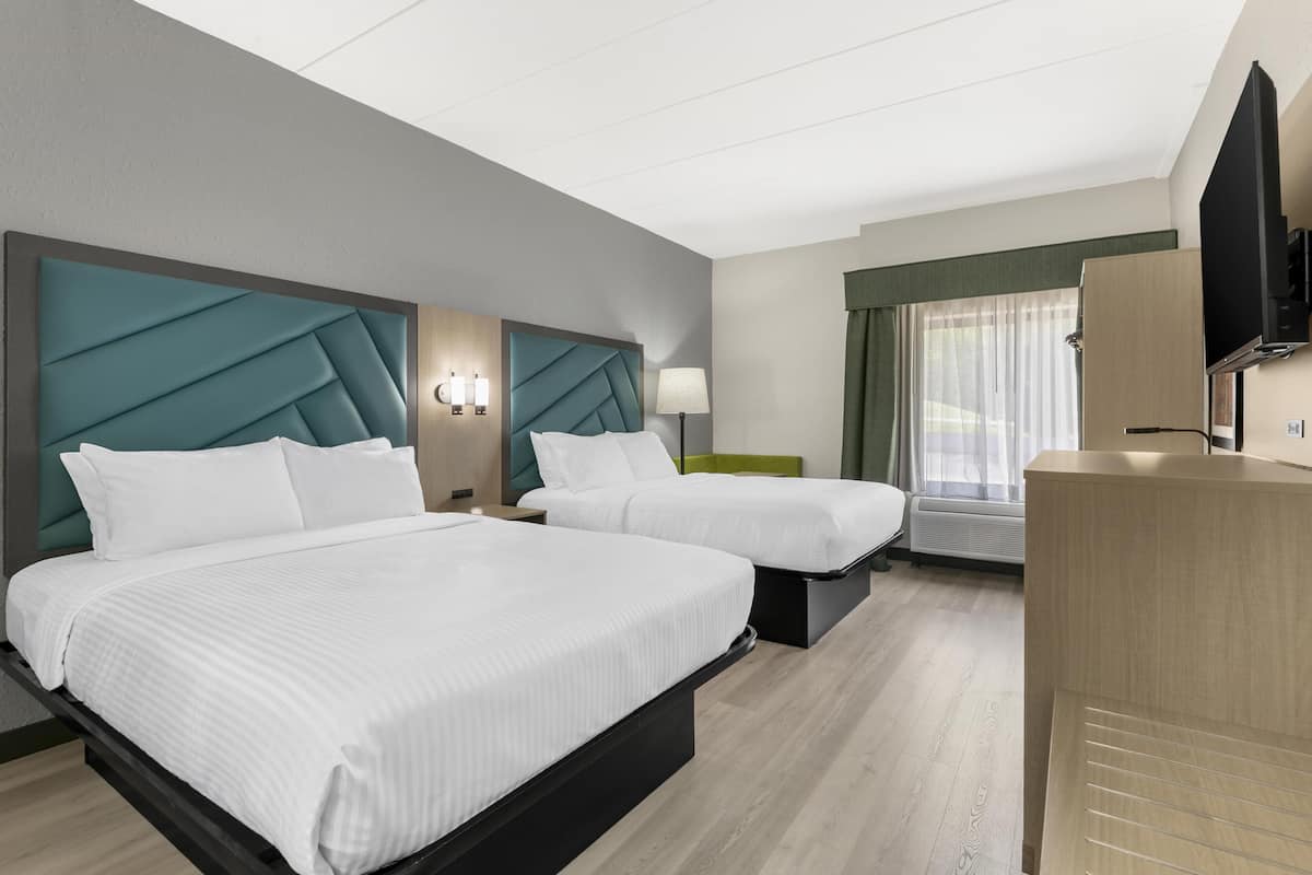 A hotel room with two beds, a TV, a desk, and a window with curtains.