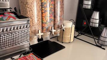 Un mostrador de aperitivos con dispensadores de cereales y dulces, una máquina para gofres y una caja de caramelos de la marca Smucker's.