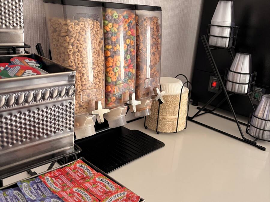 Un mostrador de aperitivos con dispensadores de cereales y dulces, una máquina para gofres y una caja de caramelos de la marca Smucker's.