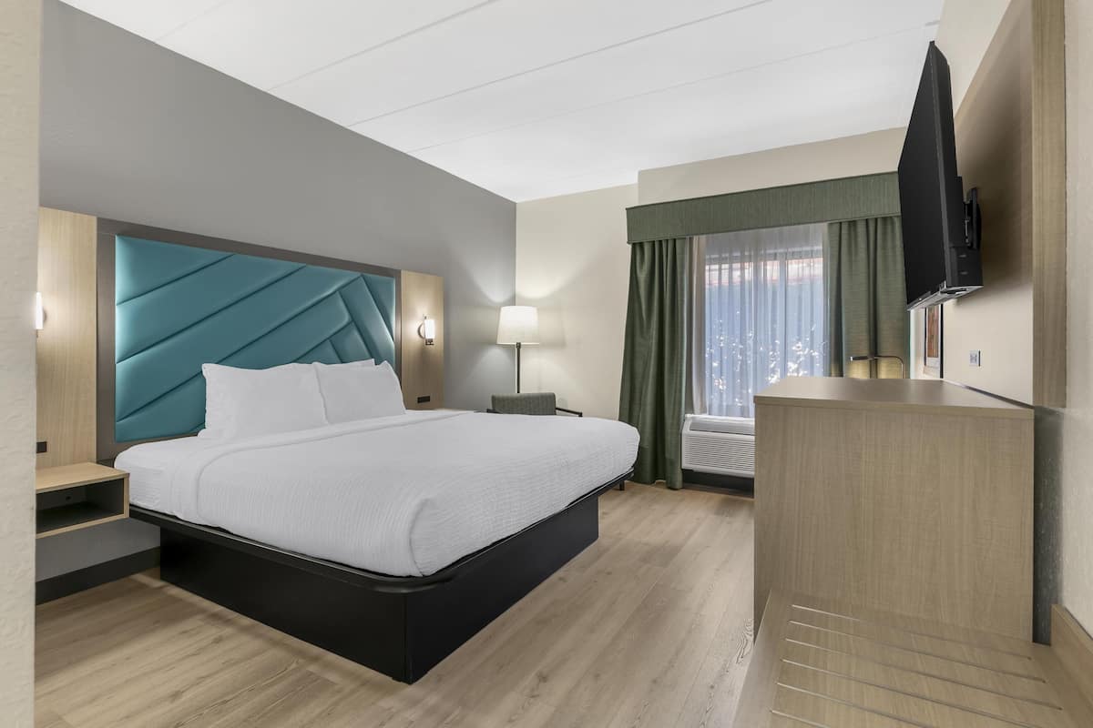 A modern hotel room with a large bed, a desk, a flat-screen TV, and a window with curtains.