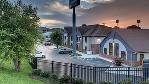 A Best Western hotel with a parking lot, a fence, and a row of townhouses in the background. - Best Western Eagles Inn (Morehead)