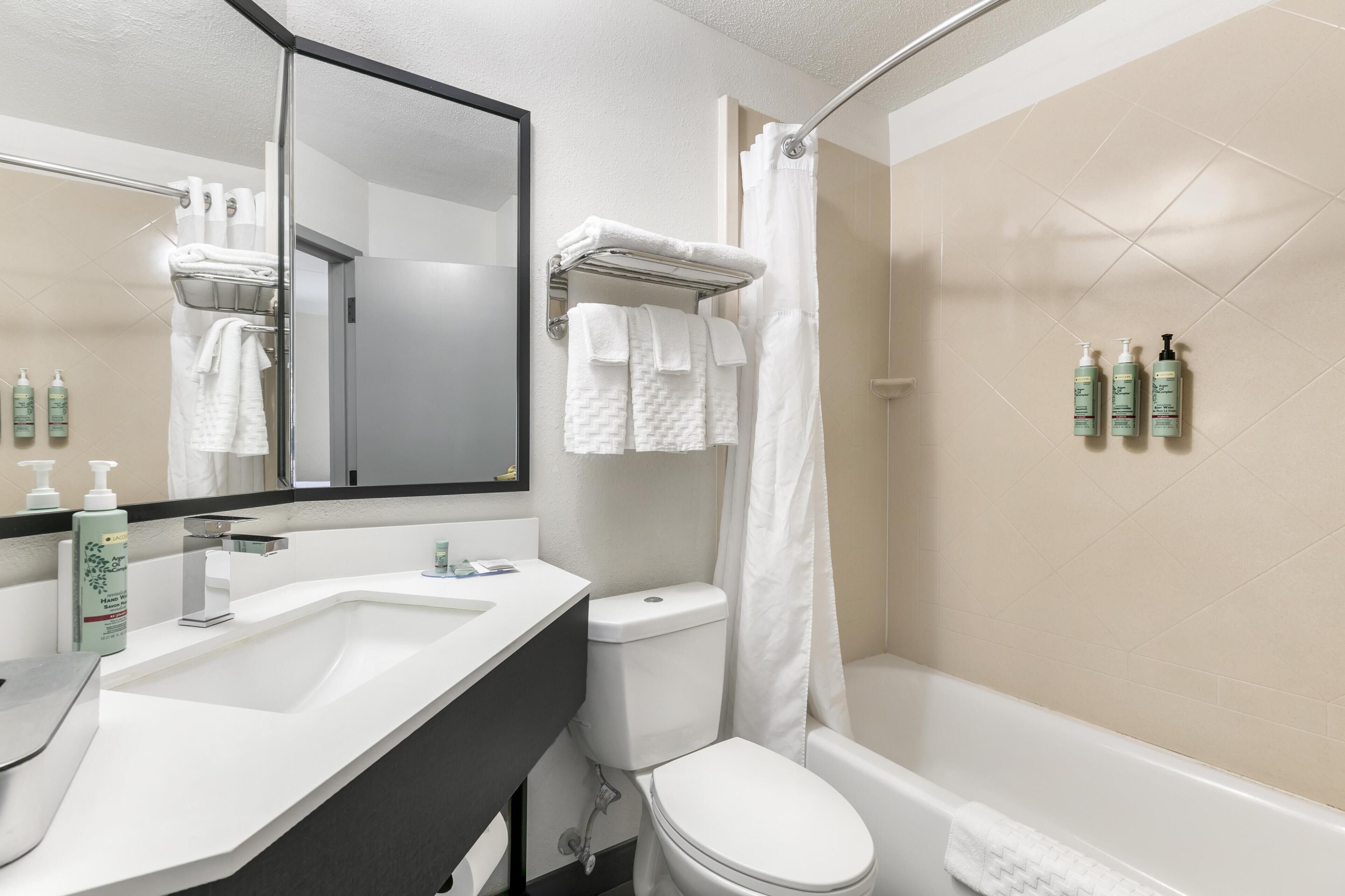 A bathroom with a sink, toilet, and bathtub. There are towels and toiletries on the wall.