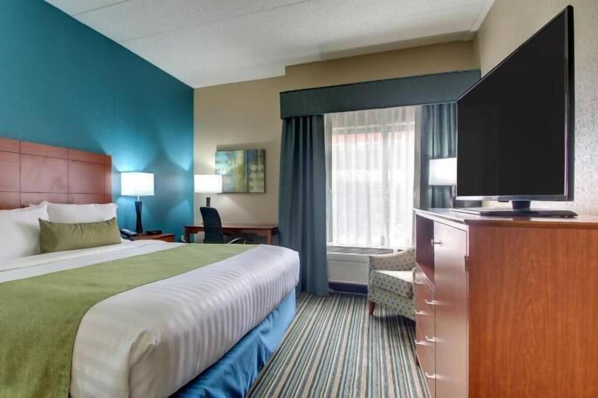 A hotel room with a large bed, a desk, a television, and a window with curtains.