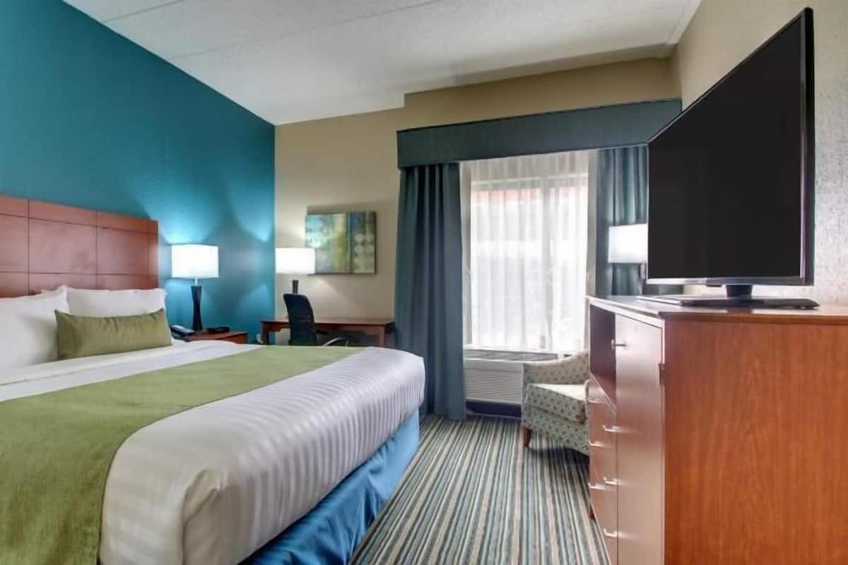 A hotel room with a large bed, a desk, a television, and a window with curtains.