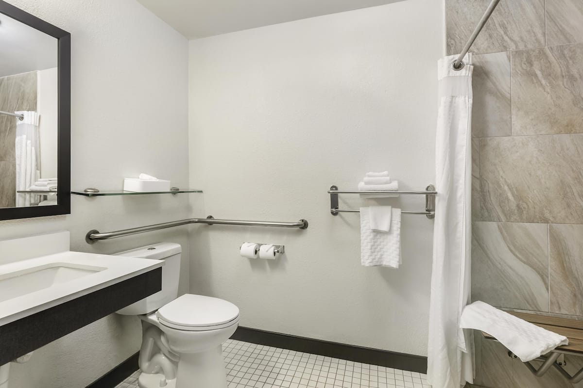 A bathroom with a toilet, sink, mirror, towel rack, and shower curtain.