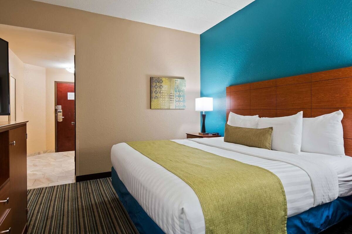 A hotel room with a bed, a TV, a painting, and a lamp.