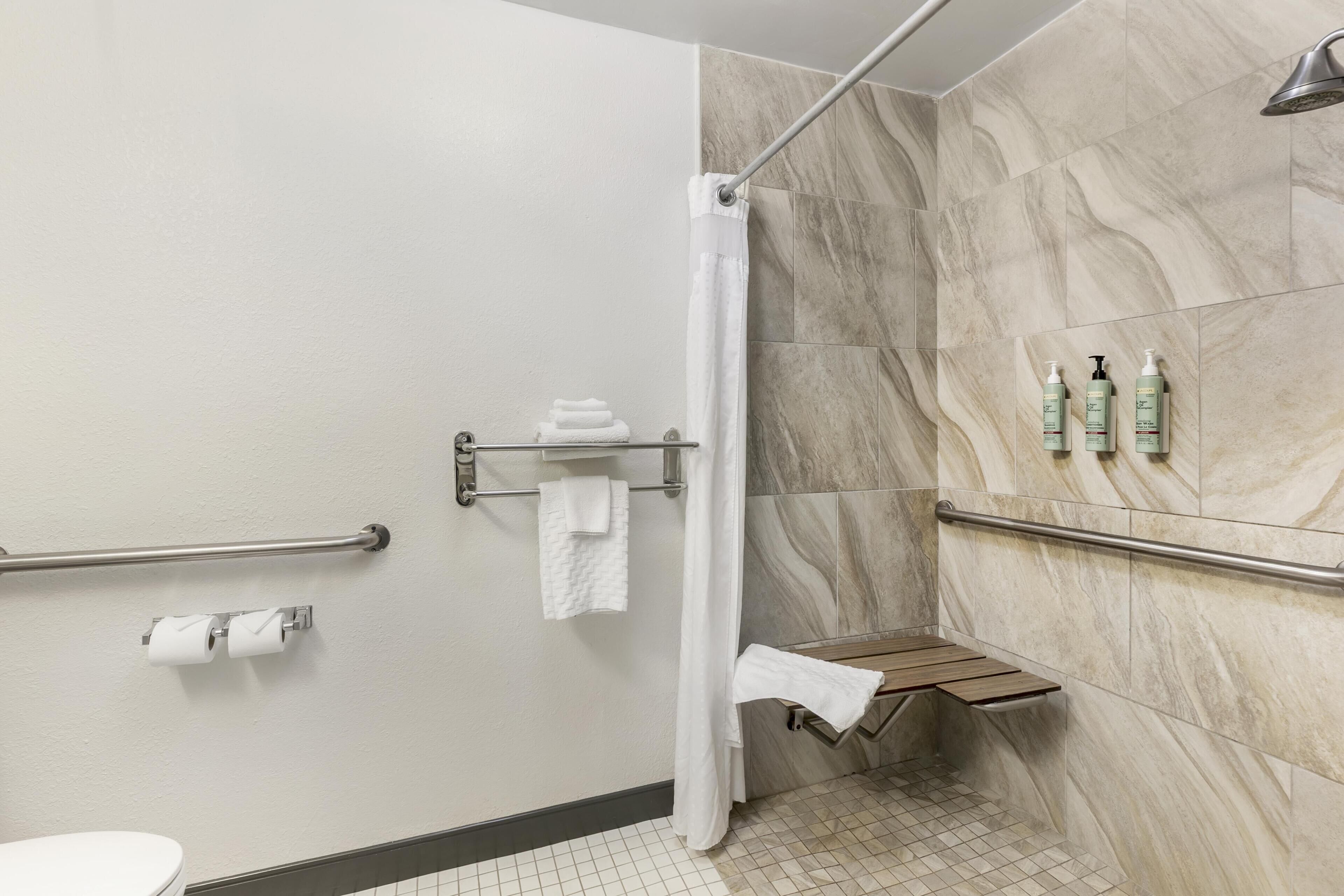 Un baño con ducha, inodoro y barras de apoyo.