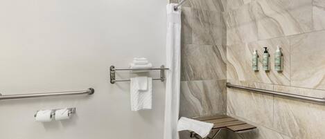 Un baño con ducha, inodoro y barras de apoyo.