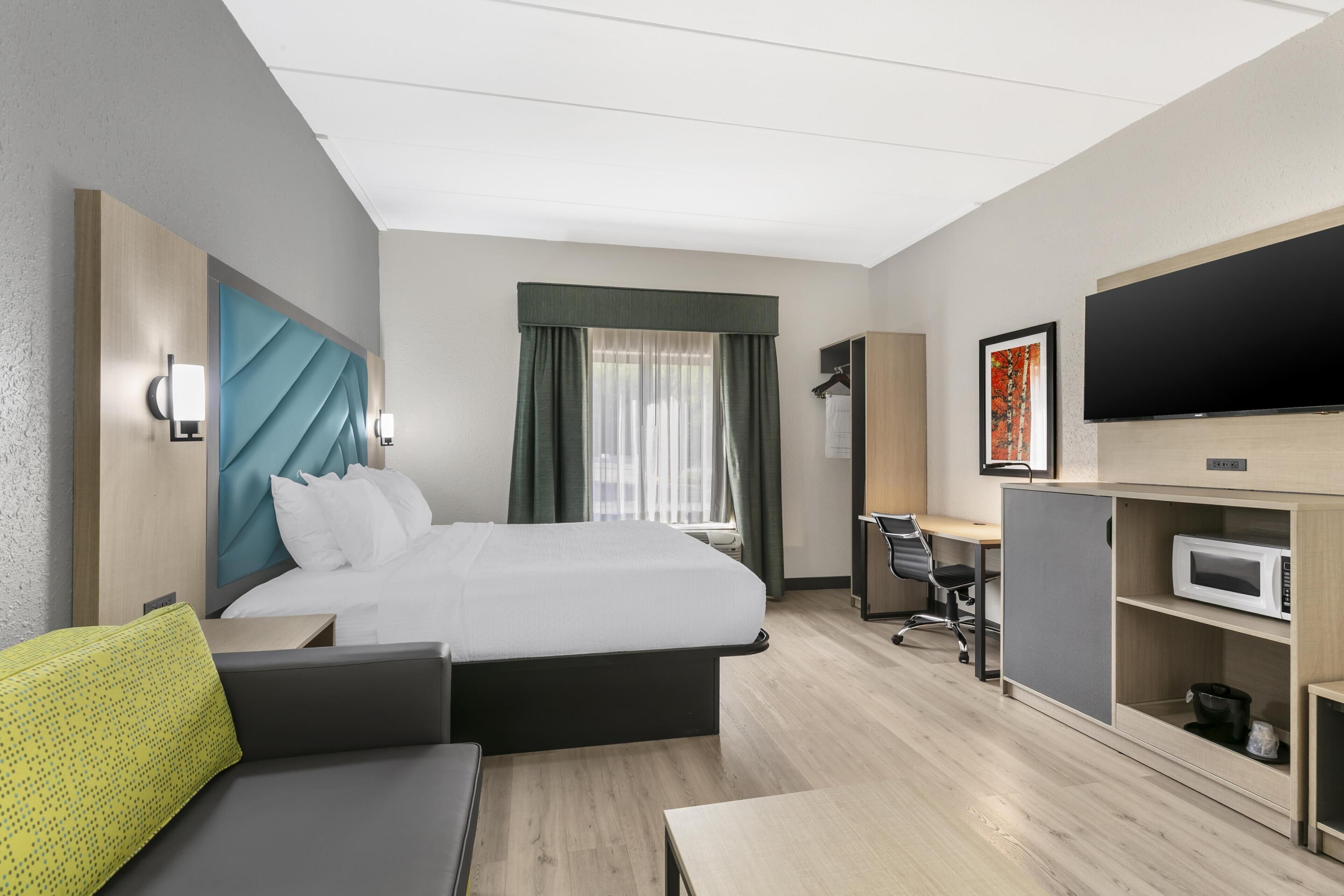 Ett modernt hotellrum med en säng, ett skrivbord, en tv och en mikrovågsugn.