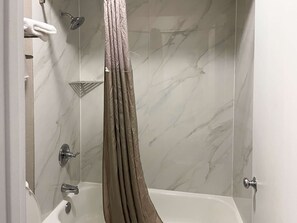 A modern bathroom with a shower curtain, a bathtub, and a handheld showerhead. - Motel 6 Baton Rouge, LA - Southeast (Baton Rouge)