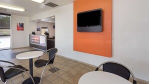 Et moderne interiør med et fladskærms-TV monteret på en orange væg, en receptionsdisk og et siddeområde med borde og stole.