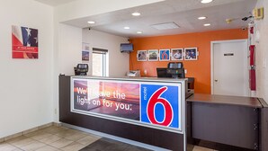 Et hotelreceptionsområde med et stort skilt, der siger "Vi lader lyset brænde for dig", og et nummer "6", der angiver motellet.