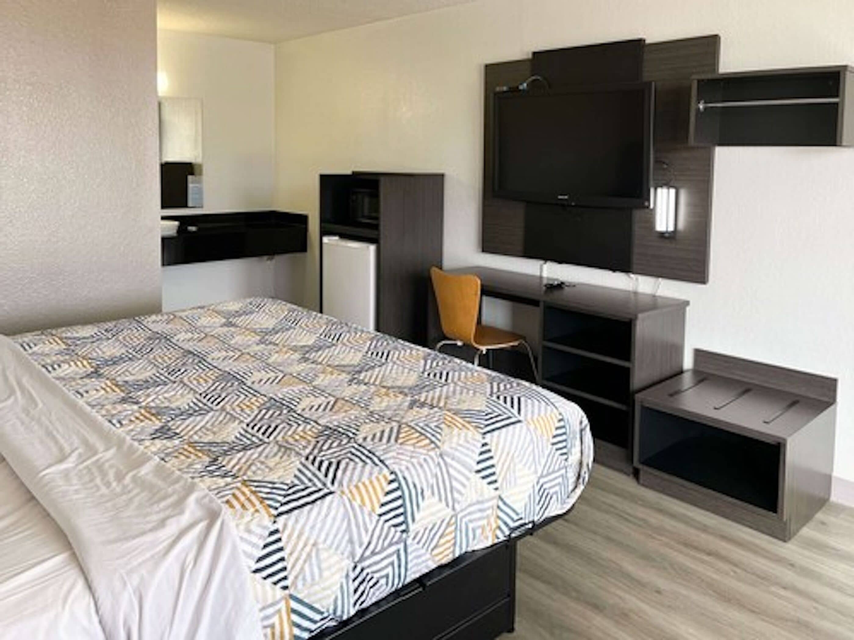 A hotel room with a bed, a desk with a chair, a television, and a wardrobe.