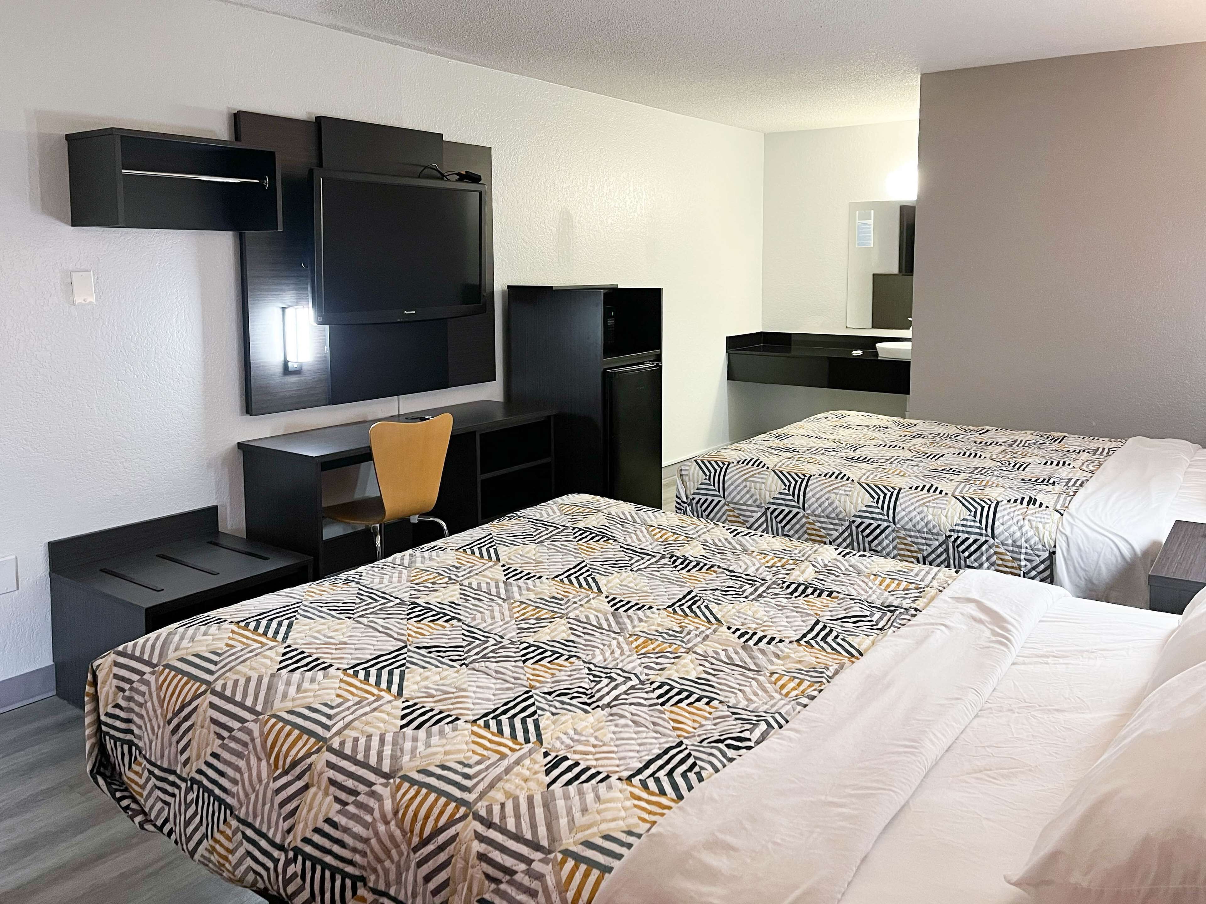 Habitación de hotel con dos camas, un escritorio, una silla, un televisor y un refrigerador.