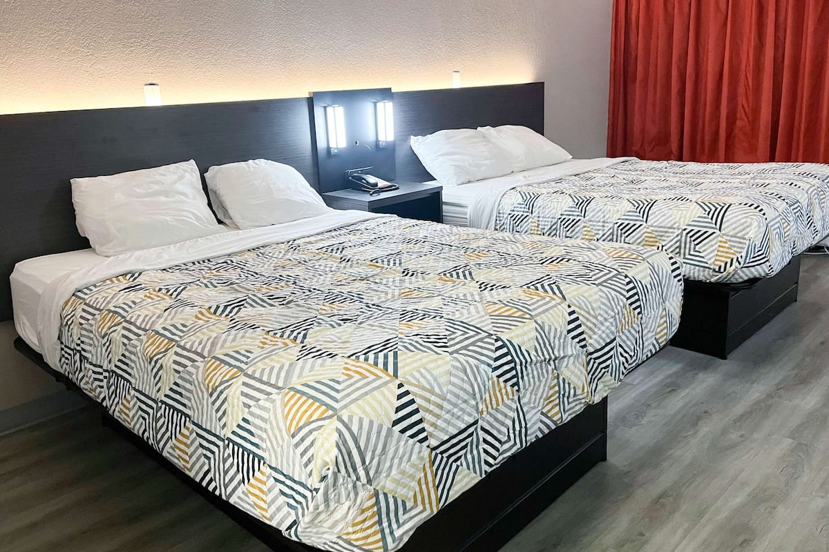 Ett hotellrum med två sängar, var och en med ett mönstrat överkast, ett sängbord med en lampa och en röd gardin.